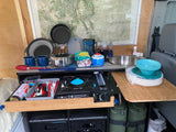 This RV rental features a well-equipped, compact camping kitchen with a stove, sink, and organized cooking supplies.