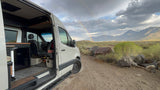 RV rental adventure: Open camper van door shows interior, with a vibrant rainbow over mountains.