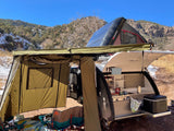 RV rental adventure: Teardrop trailer with tent extension, rooftop tent, & outdoor kitchen set up for camping in snowy mountains.
