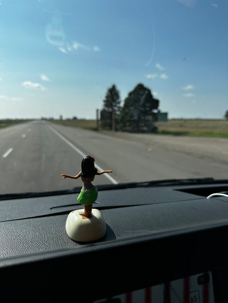 Dashboard hula girl in an rv rental, gazing at the long, empty road under a bright sky. Scenic road trip journey.