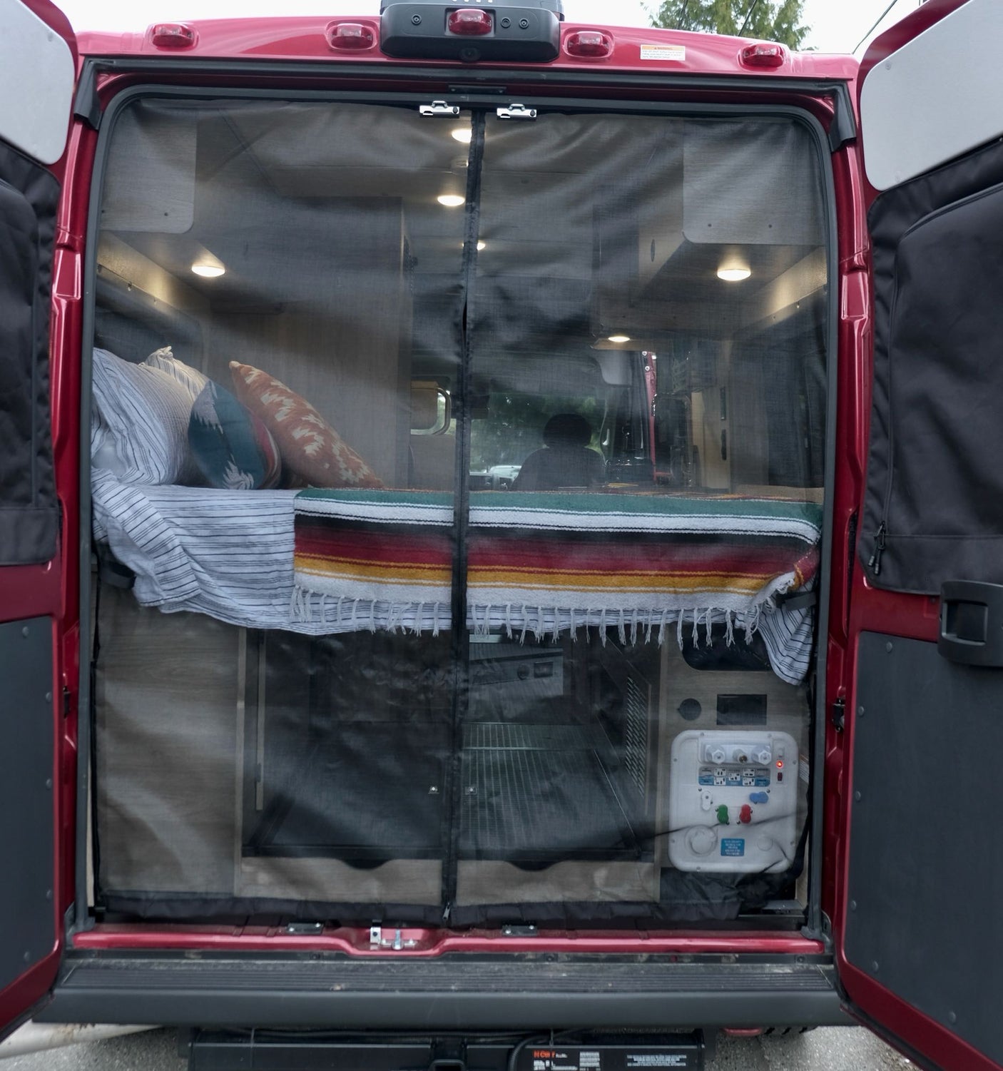 Discover comfort with this RV rental! Rear view of a camper van interior, showcasing a cozy bed and protective mesh screen.