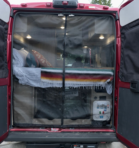 Discover comfort with this RV rental! Rear view of a camper van interior, showcasing a cozy bed and protective mesh screen.