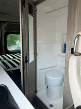 RV rental interior featuring a compact bathroom with toilet and shower, adjacent to a bed area. Functional design for travel.