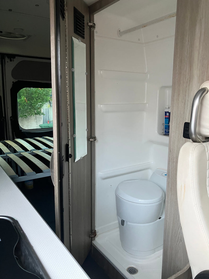 RV rental interior featuring a compact bathroom with toilet and shower, adjacent to a bed area. Functional design for travel. — photo 4