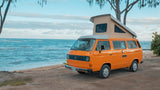 Bright orange VW pop-top camper van, perfect RV rental for beach adventures by the ocean.