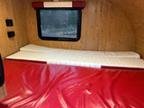 Inside an rv rental: wood interior, control panels, window, and red/white modular sleeping cushions.