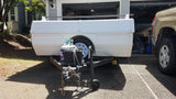 White utility trailer with propane tank and battery, parked on a driveway next to a truck. An ideal setup for an rv rental excursion.