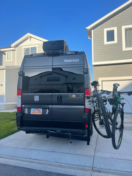 Grey Winnebago Solis **RV rental** van with bikes on a rear rack, parked in a driveway. Utah license plate visible.