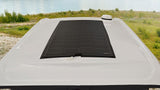 Top view of an RV rental roof with a large flexible solar panel and a white antenna, overlooking a lake.