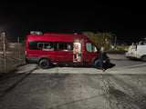 A vibrant red RV rental, ready for adventure, is pictured at night with a woman by its open side door.