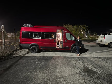 A vibrant red RV rental, ready for adventure, is pictured at night with a woman by its open side door.
