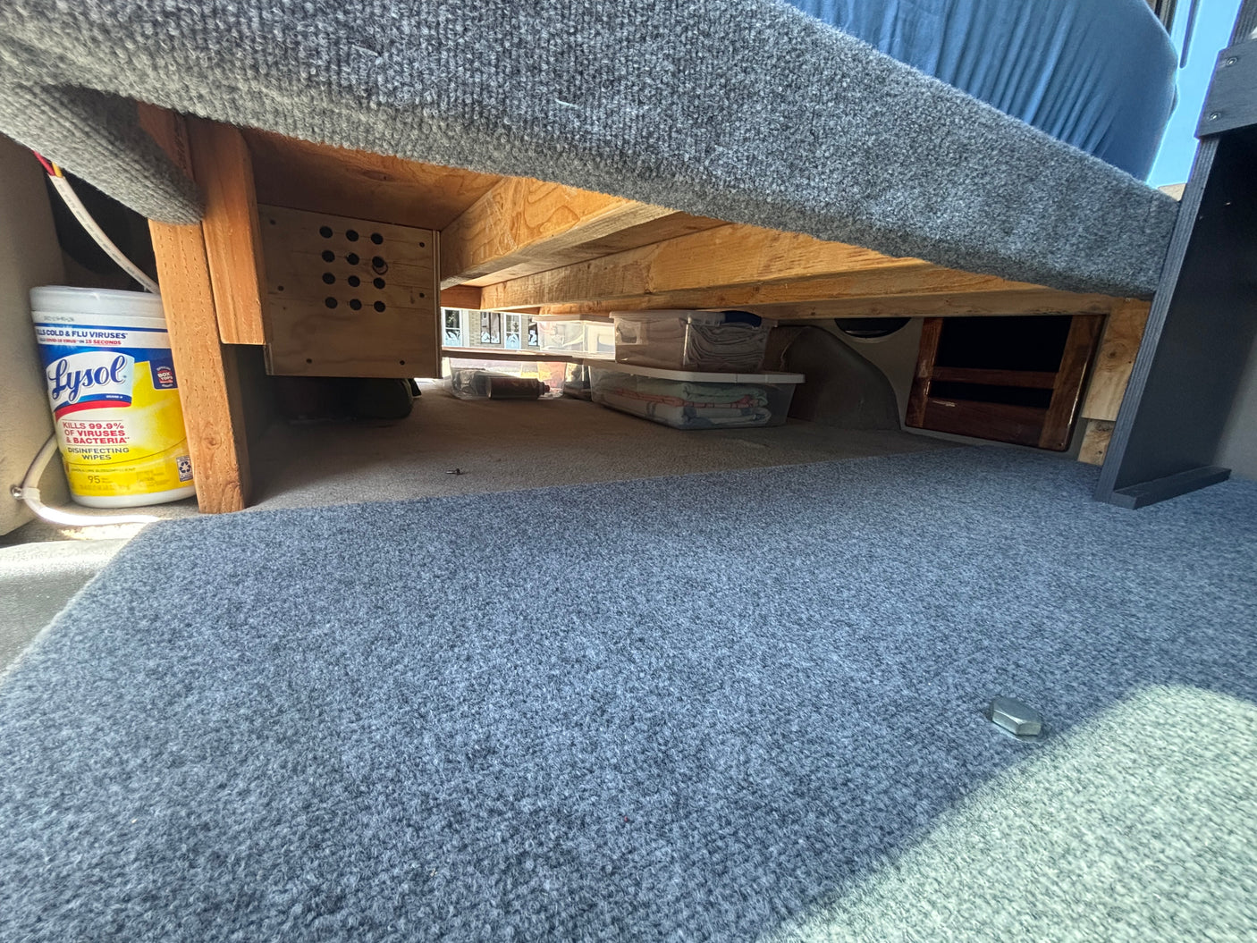 Compact RV rental interior: under-bed storage solutions with wood framing, clear bins, and Lysol wipes for travel organization.