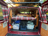Cozy RV rental camper van interior: plaid bed, under-bed storage, and wood paneling. Ready for adventure!