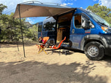 Enjoying the outdoors from a blue camper van with awning. Ideal for your next RV rental adventure!