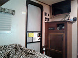 This RV rental interior shows a bed with zebra print, window, entry door, TV, and wood storage cabinet with a fire extinguisher.