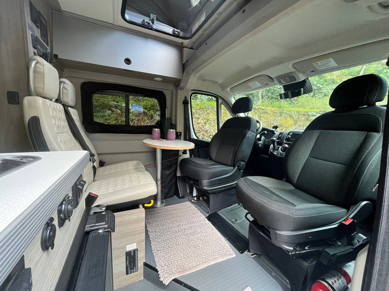 View inside an RV rental showing the living space. Features front swivel seats, a dining area with table & bench seats, and a compact kitchen. — photo 7
