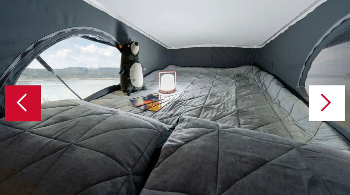 This RV rental offers a cozy camper bed with soft grey blankets, featuring a beautiful lakeside view from the large window. — photo 18
