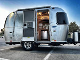 Airstream RV rental: Silver travel trailer with open door showing interior kitchenette and fridge. Parked, ready for adventure.