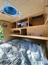 Inside a cozy RV rental: quilted bed, built-in storage with nets & lantern, plus a ceiling fan.