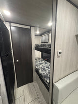 RV rental interior: two bunk beds, refrigerator, and light couch, showcasing a compact and functional layout.