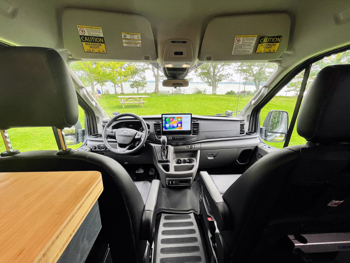 This RV rental offers a dashboard view of a serene lake and picnic area, ideal for scenic trips.