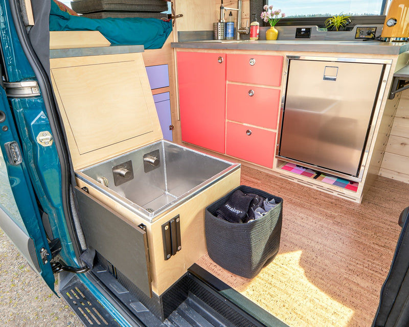 This RV rental offers a well-designed interior with a functional kitchen, colorful cabinets, built-in fridge, and creative storage solutions. — photo 14