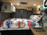 Step into this RV rental! A cozy bed with playful camper designs, compact kitchen sink, overhead cabinets, and wood interior.