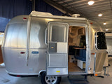 A silver Airstream Bambi travel trailer with an open door, revealing its cozy interior. Great for your next rv rental.