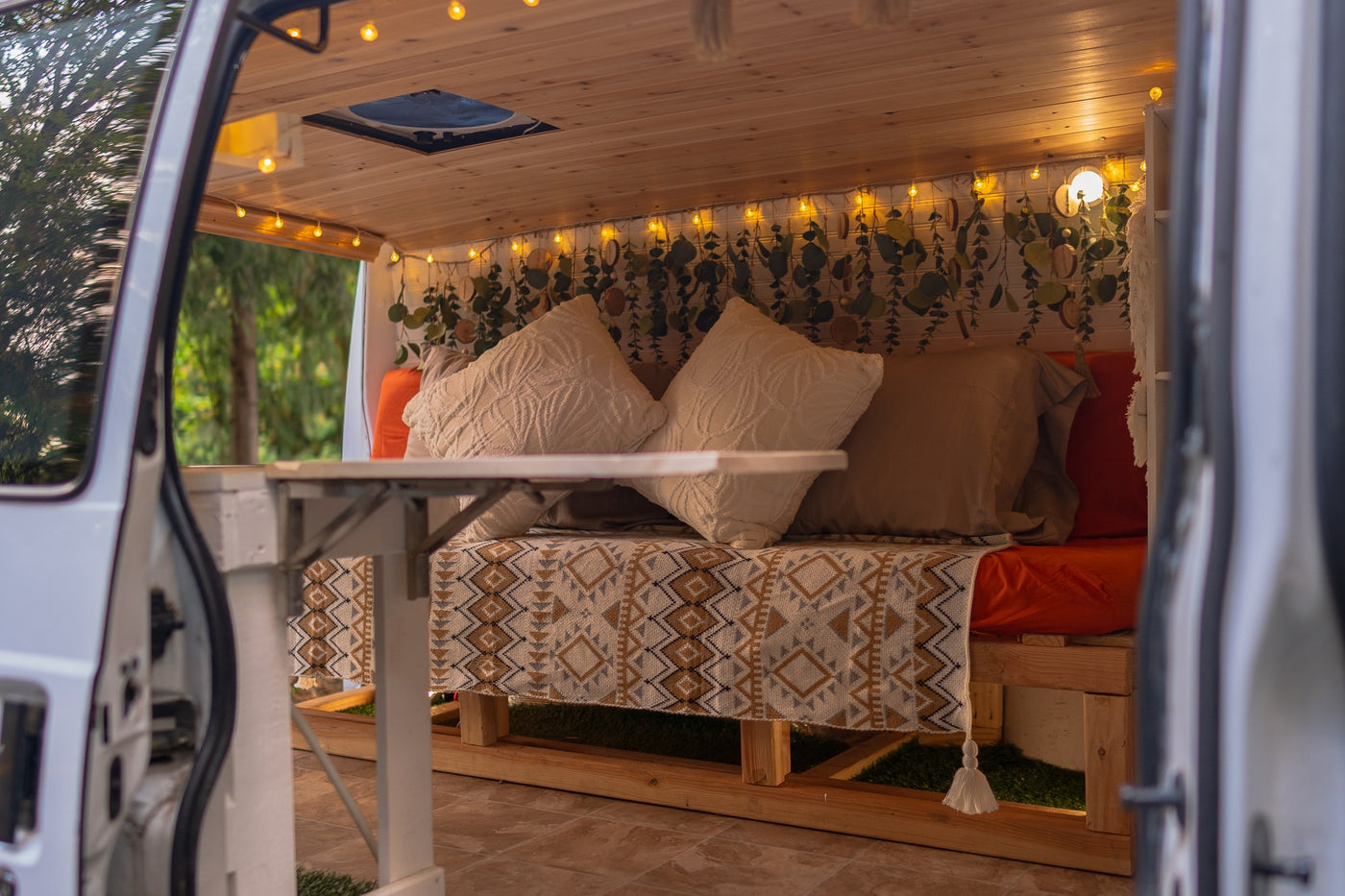 An inviting RV rental interior: cozy bed with decorative pillows, string lights, and hanging greenery. — photo 7