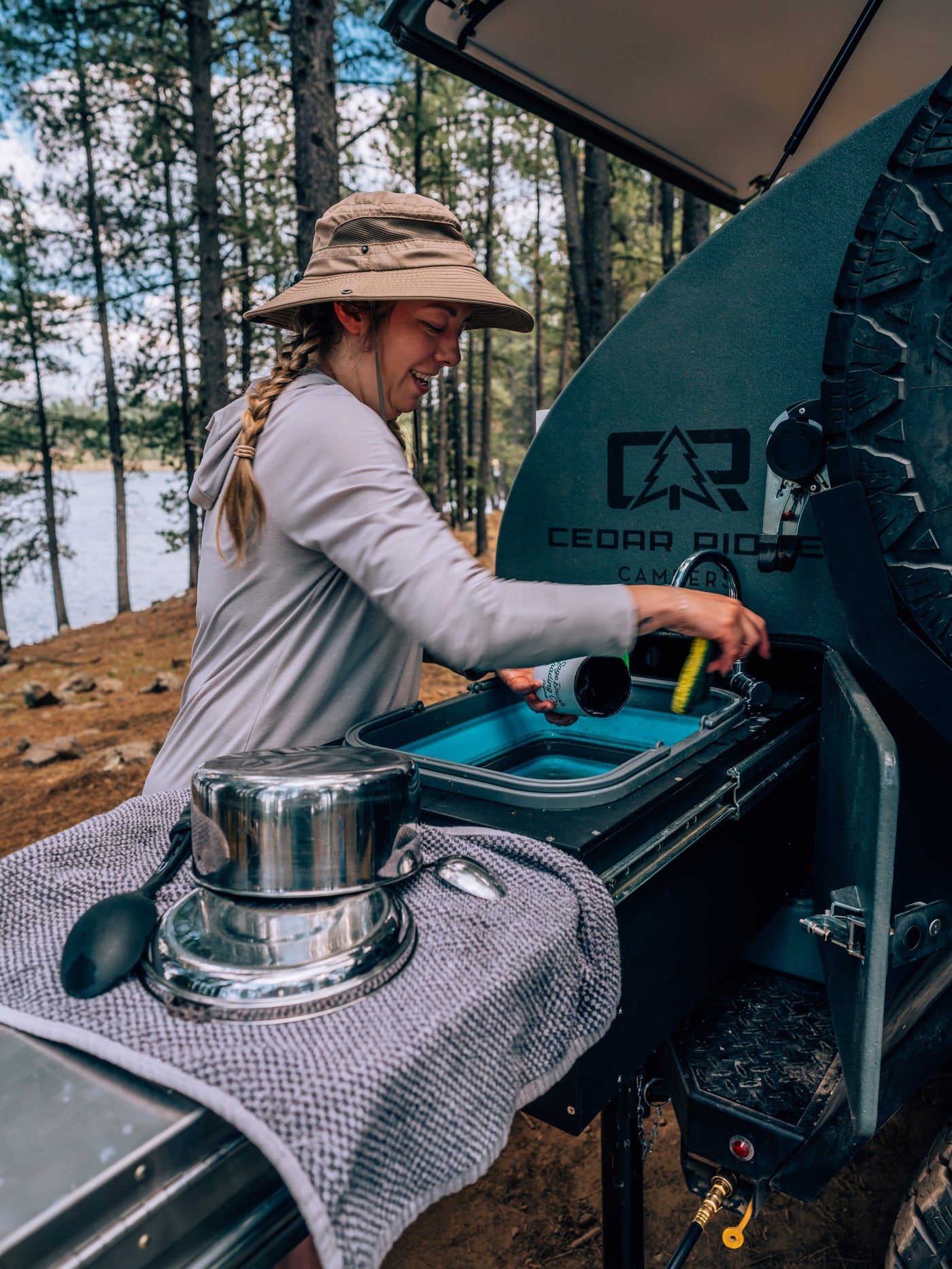 Making the most of an RV rental: a woman washes dishes at a portable Cedar Ridge camper kitchen with a lake view. — photo 4