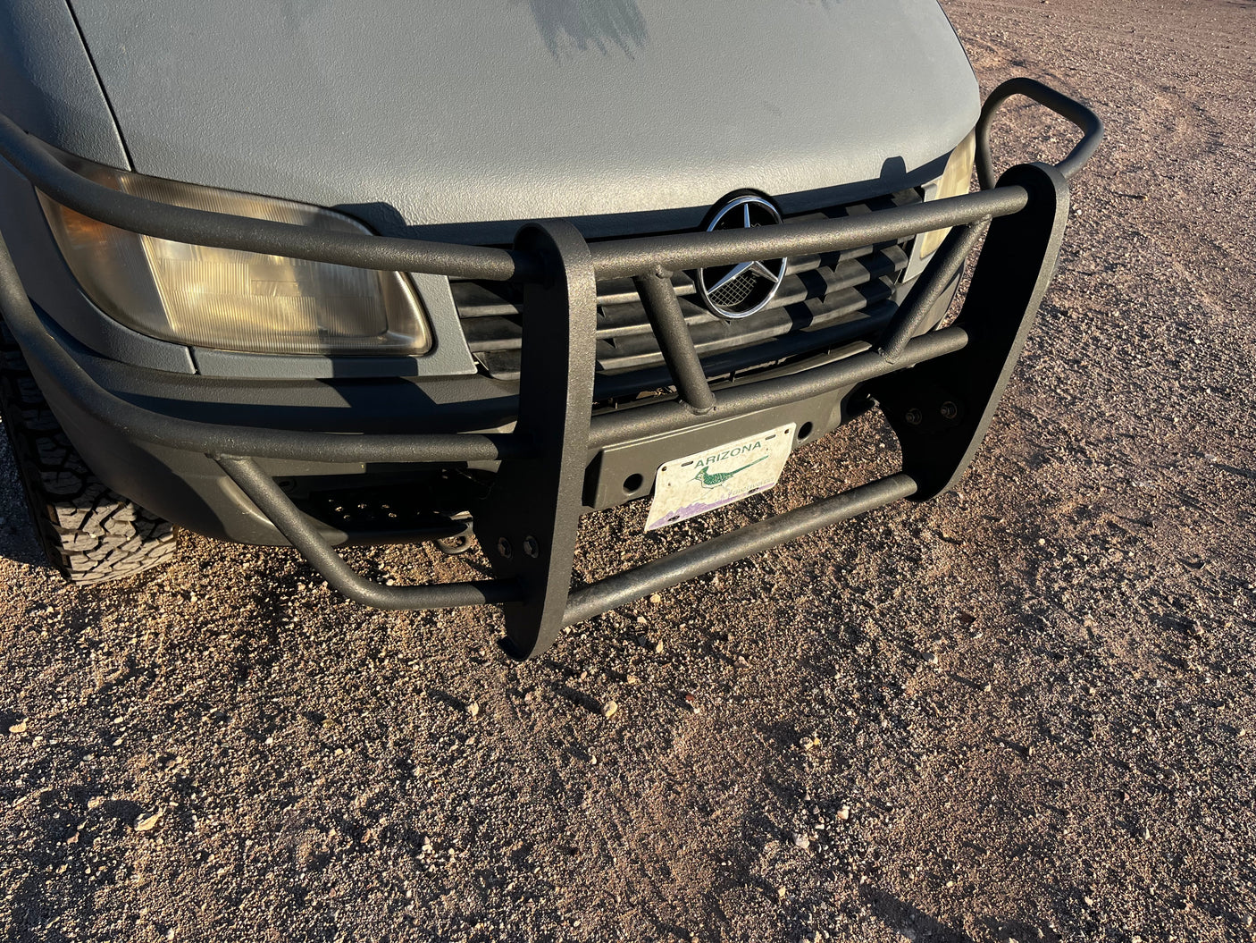 Textured gray Mercedes-Benz Sprinter rv rental with a heavy-duty brush guard, Arizona license plate, and off-road tires.