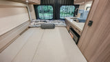 Interior of an RV rental with a cozy bed, kitchen featuring a sink, cooktop, coffee maker, and microwave, perfect for camping.
