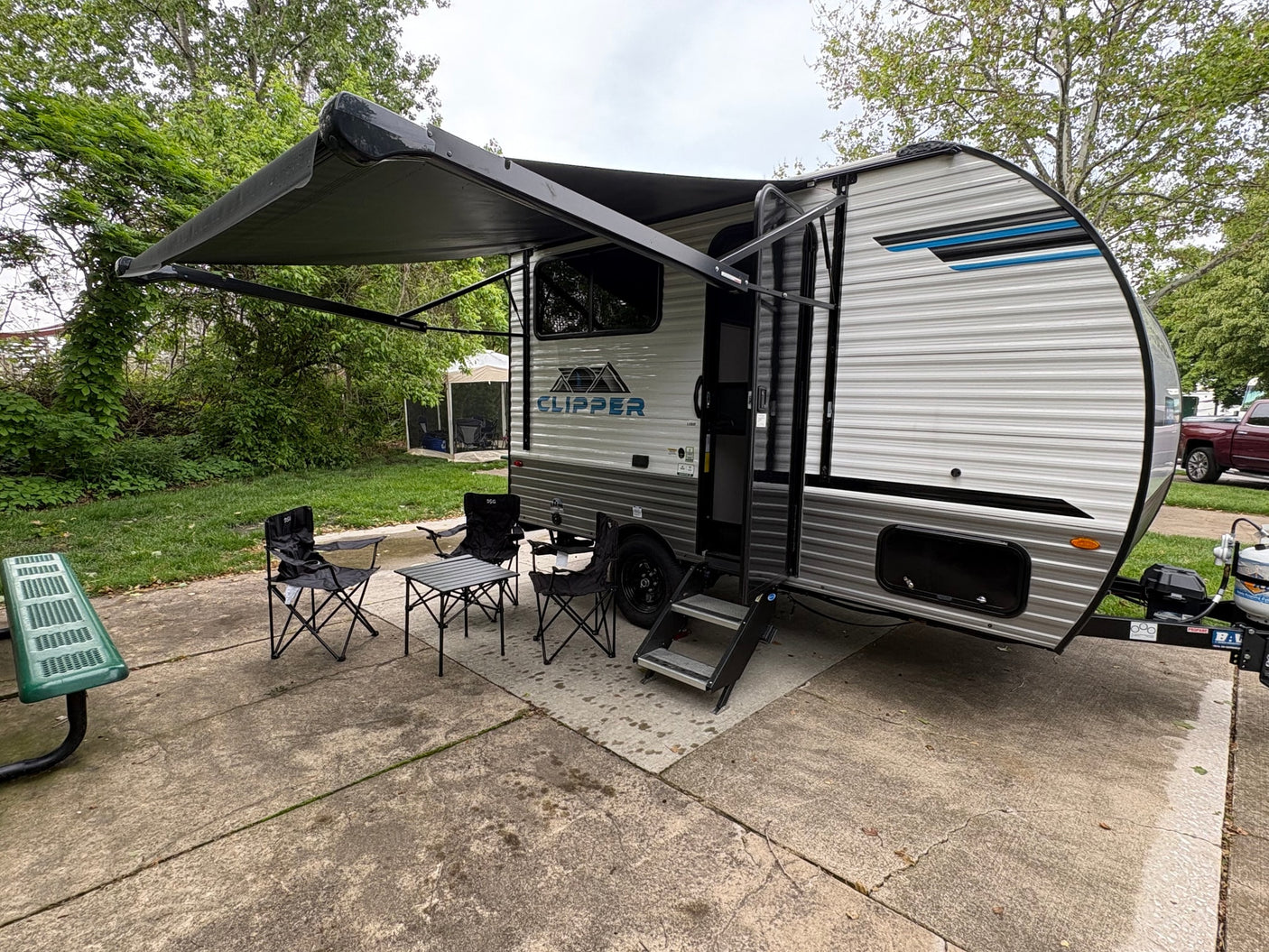 This Clipper RV rental features an extended awning, outdoor chairs, and a table on a concrete pad, ready for camping.