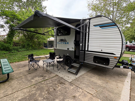 This Clipper RV rental features an extended awning, outdoor chairs, and a table on a concrete pad, ready for camping.