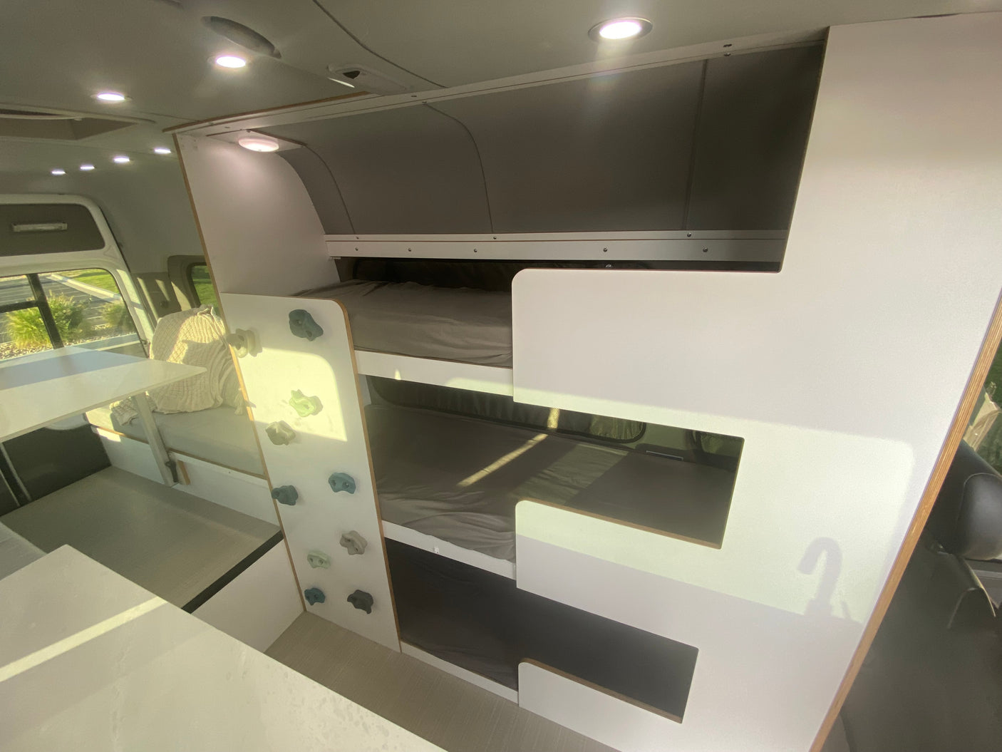 Inside a modern **rv rental**: bunk beds with a fun climbing wall, plus a comfortable dining/seating area.