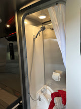 Step into this RV rental's compact, well-lit shower area, featuring a shower head, small sink, and fresh towels for your journey.