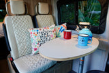 This RV rental interior shows plush seating, a table with a kettle and mugs, ideal for comfortable travel and camping.