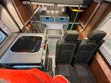 RV rental interior: Person's leg in foreground, rear seats, kitchenette, blue-drawer storage, and overhead bed.