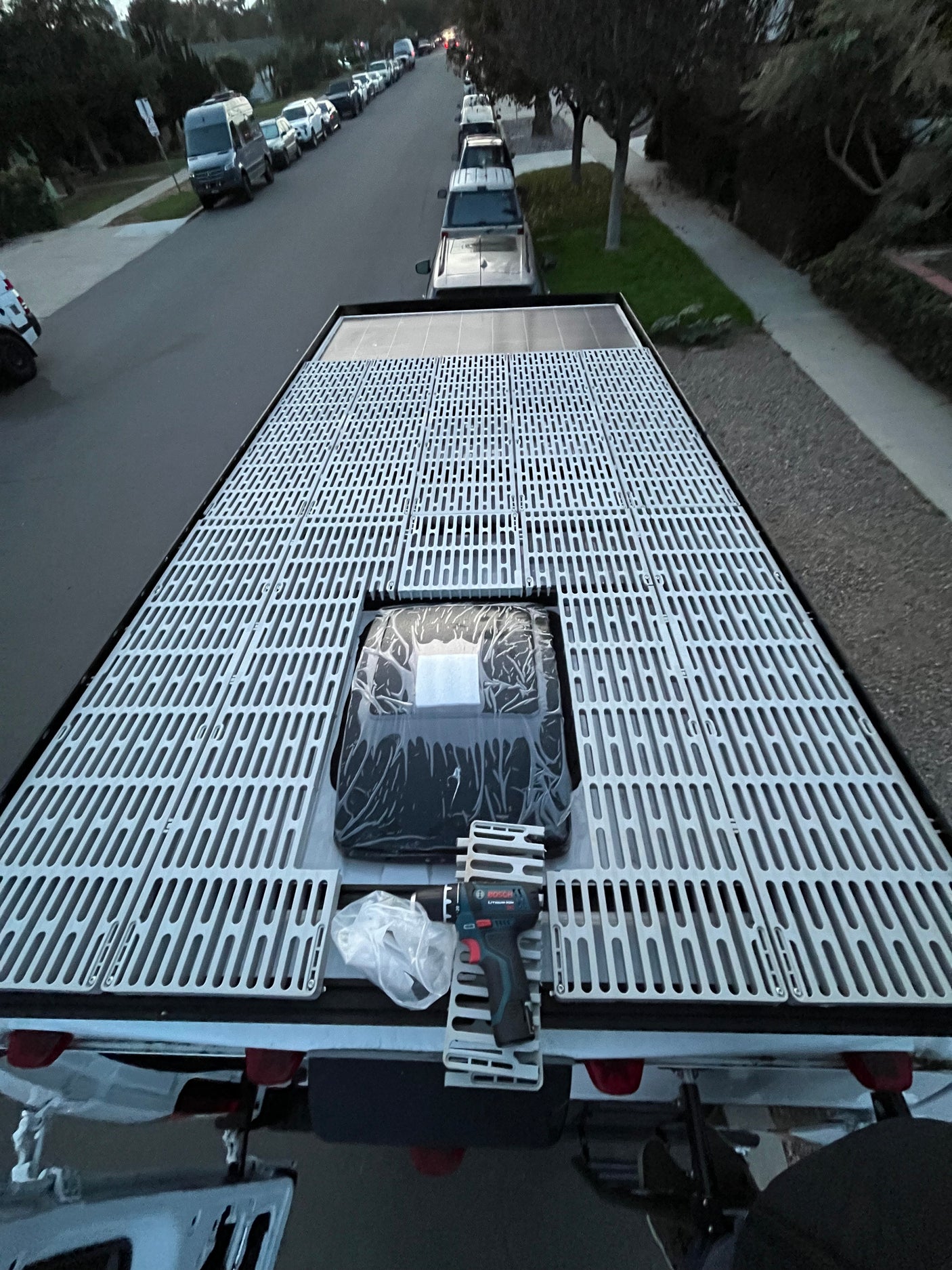 Overhead view of an RV rental roof with a custom slatted deck, solar panels, and a drill, parked on a street.