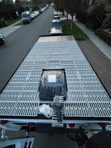 Overhead view of an RV rental roof with a custom slatted deck, solar panels, and a drill, parked on a street.
