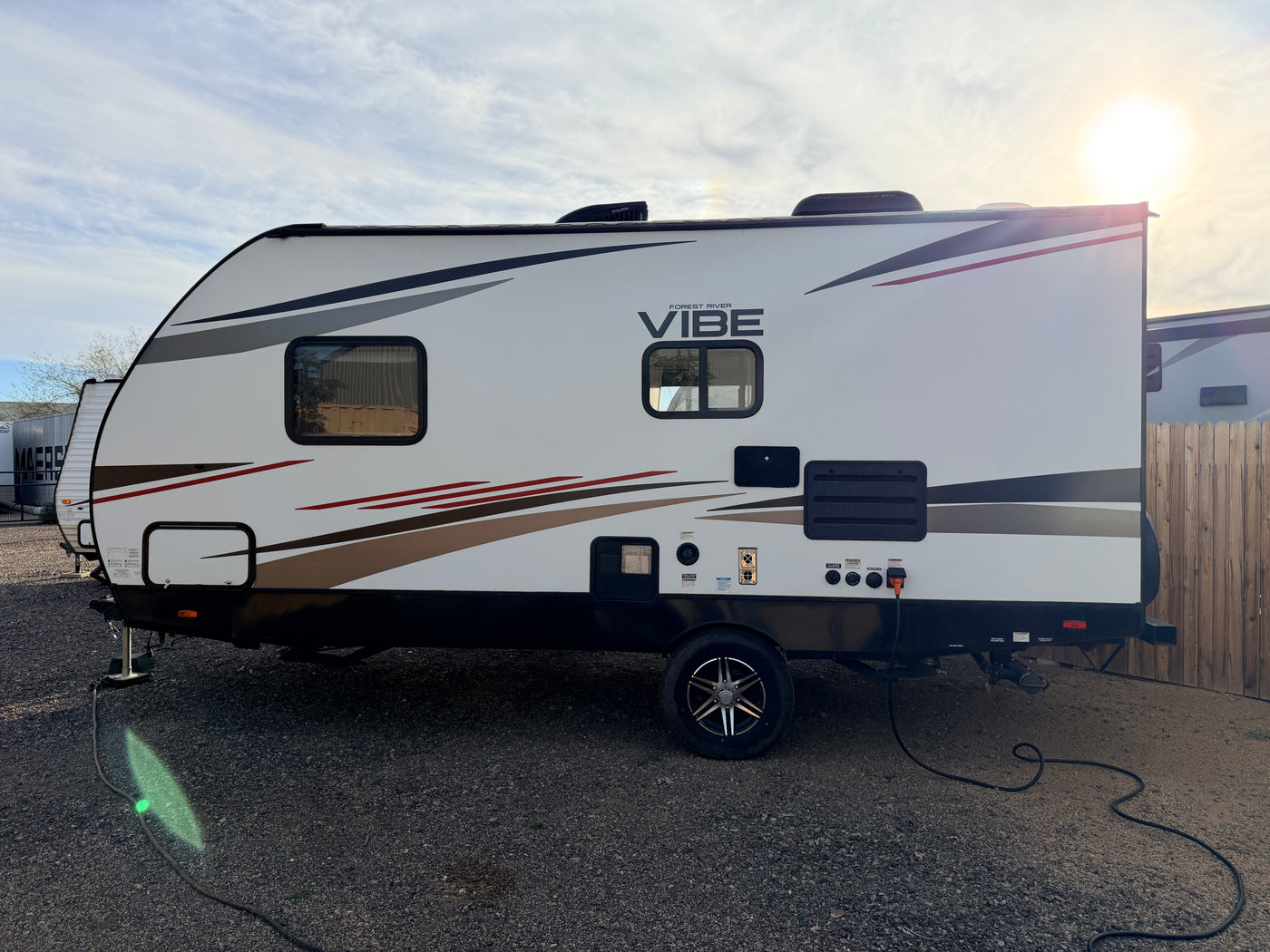 A clean white Forest River Vibe travel trailer, perfect for an RV rental, parked on gravel with power connected. — photo 15