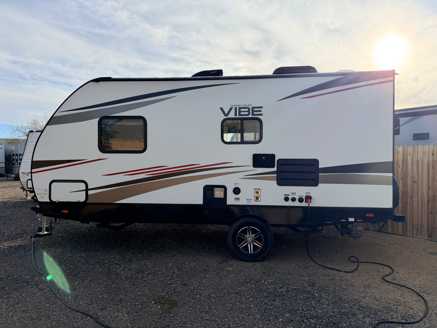 A clean white Forest River Vibe travel trailer, perfect for an RV rental, parked on gravel with power connected.