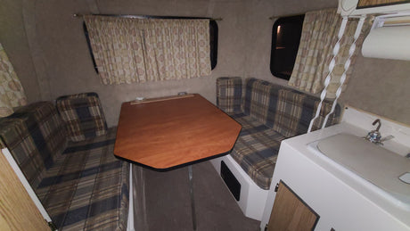 Explore this clean rv rental interior: A dinette with plaid benches, wooden table, and sink area awaits.