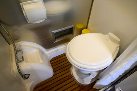 Compact RV rental wet bath with toilet, shower, wooden slatted floor, and wall-mounted toilet paper dispenser.