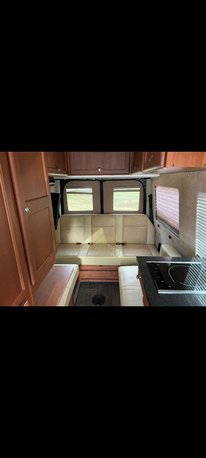 Inside this modern RV rental: light bench seating, wood cabinetry, and a compact kitchen with a cooktop. — photo 6