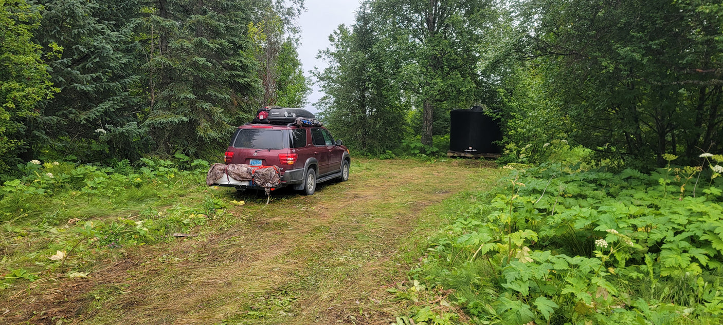 Adventure-ready SUV, packed like an RV rental for wilderness travel, parked in lush woods with a water tank.