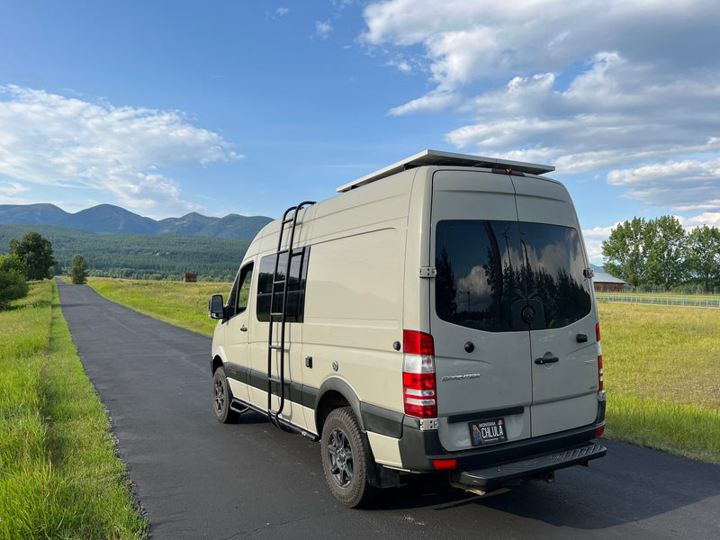 A beige Sprinter camper van, equipped with solar panels and a ladder, parked on a paved road in scenic Montana. Ideal for an RV rental experience. — photo 4