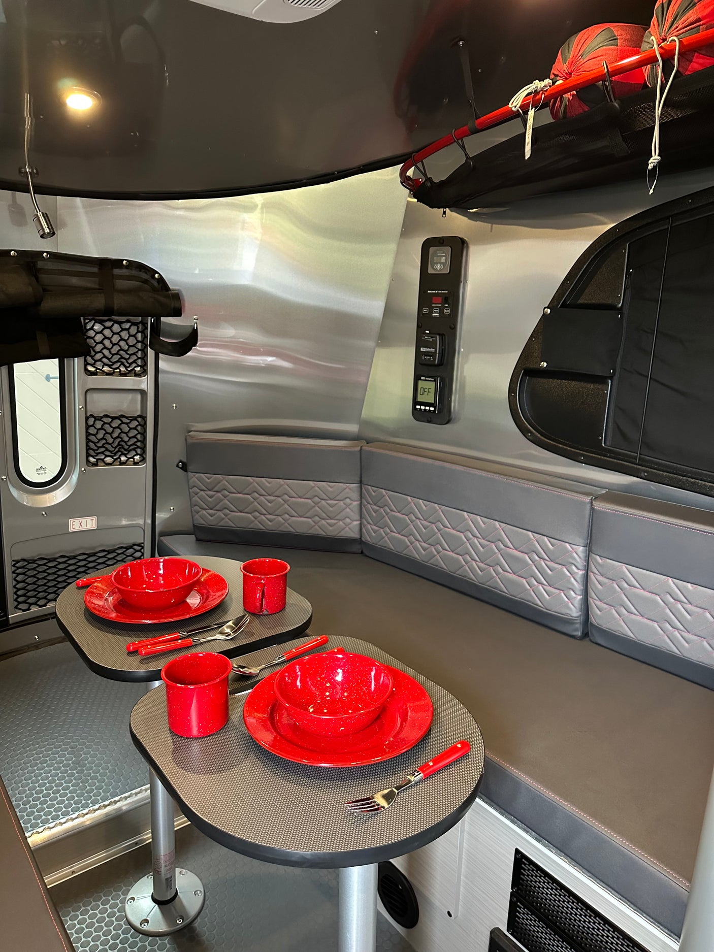 Modern RV rental interior: compact dinette with red dishware, cozy seating, and smart storage.