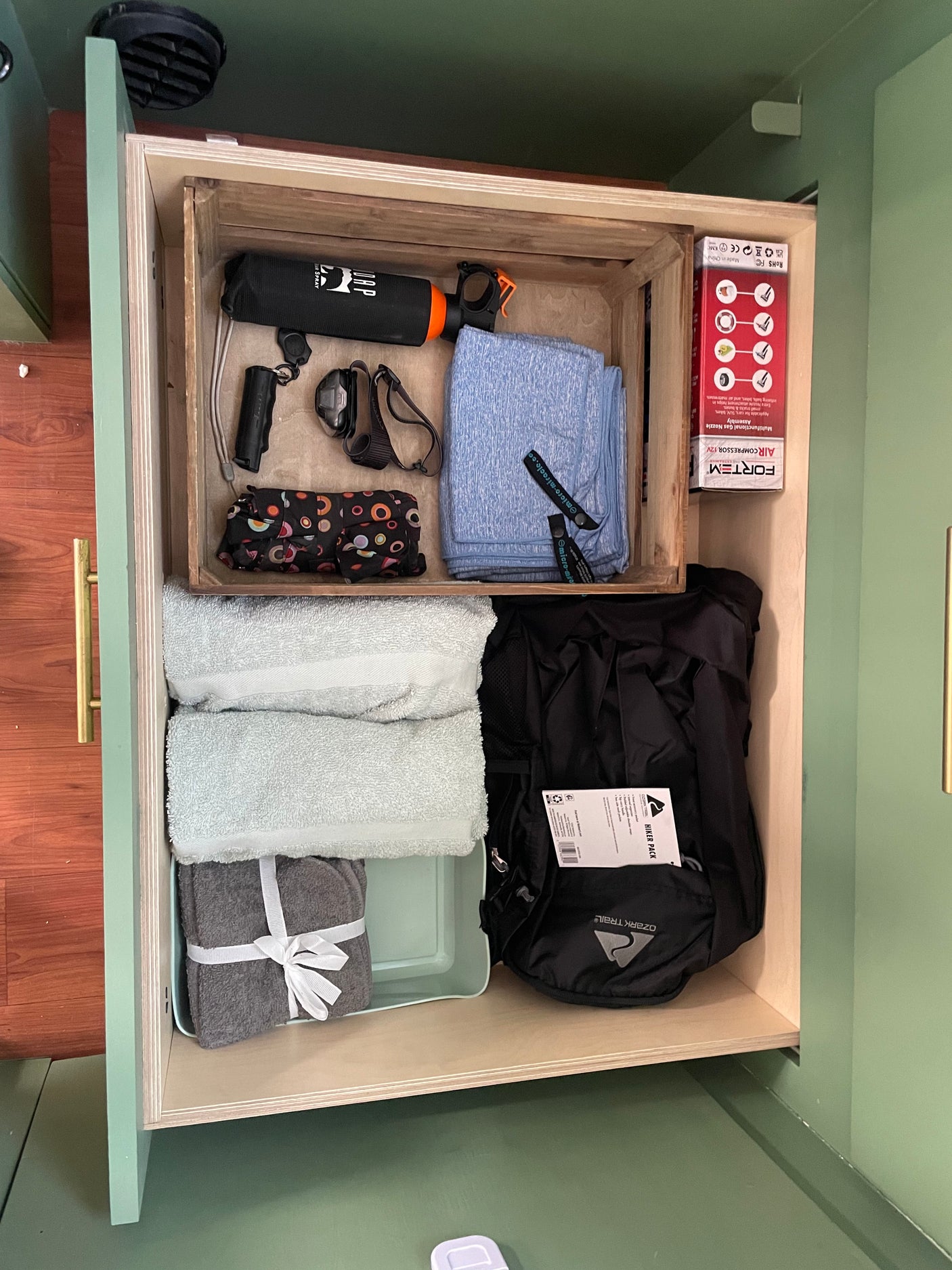 RV rental storage: An organized pull-out drawer filled with towels, an air compressor, bear spray, and a hiker pack for travel adventures.