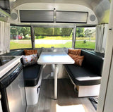 RV rental interior shows a bright Airstream dinette with black benches, a white table, and large windows looking out.